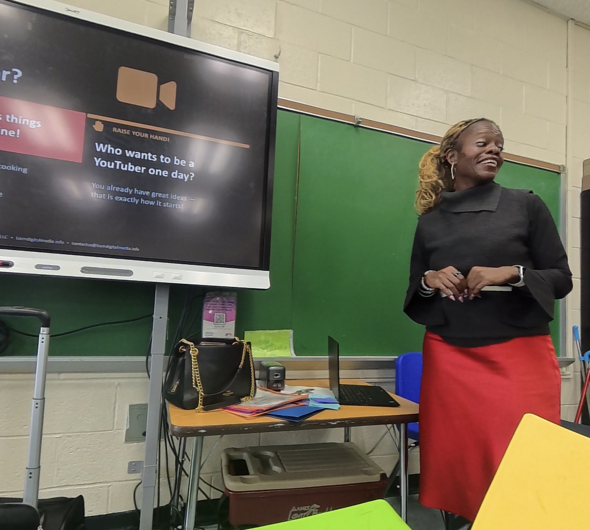 Schnelle Acevedo teaching a classroom lesson with a slide asking Who wants to be a YouTuber one day