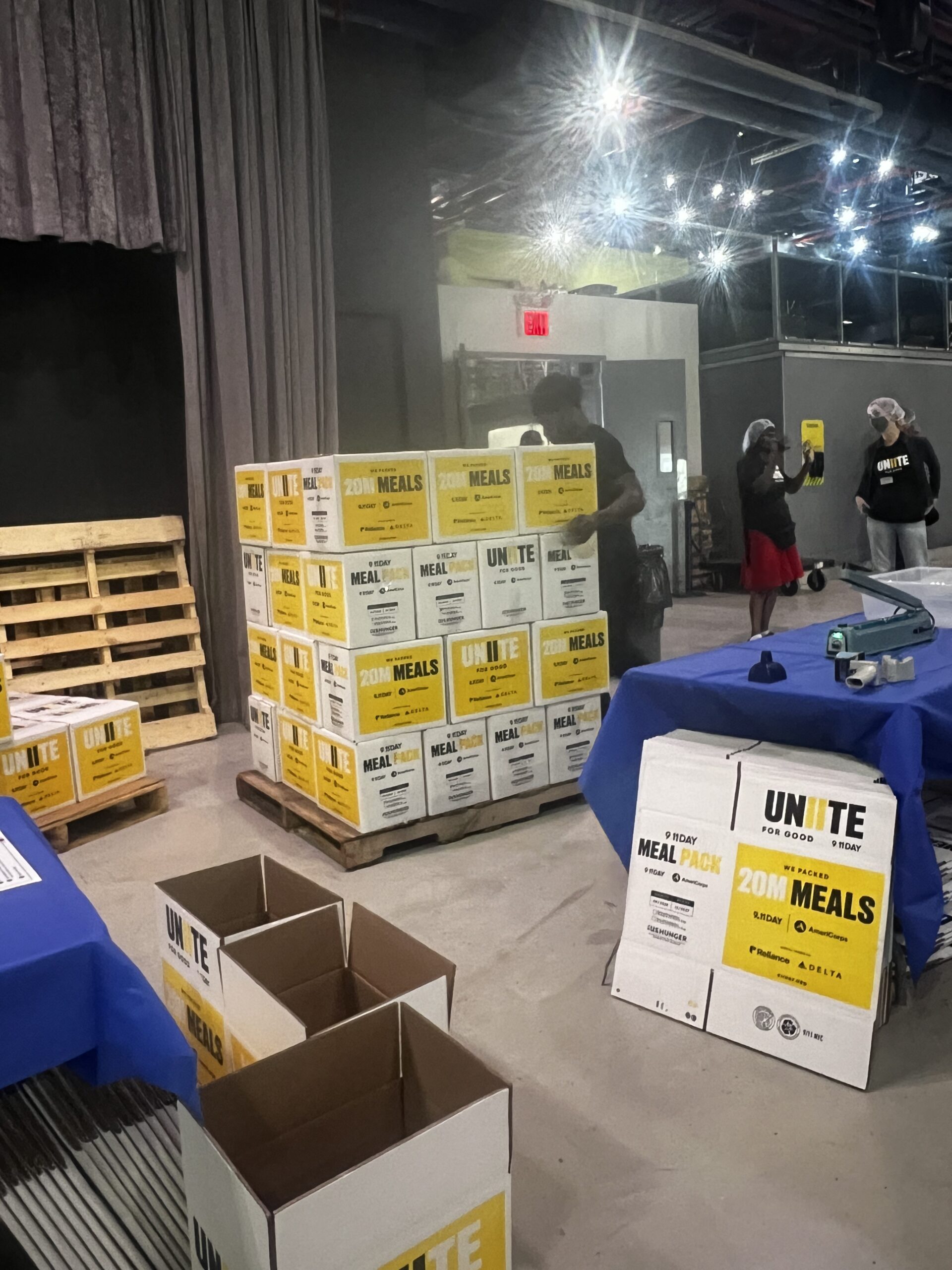 Stacked pallets of packed meal boxes labeled UNIITE For Good, 20M Meals, 9.11 Day