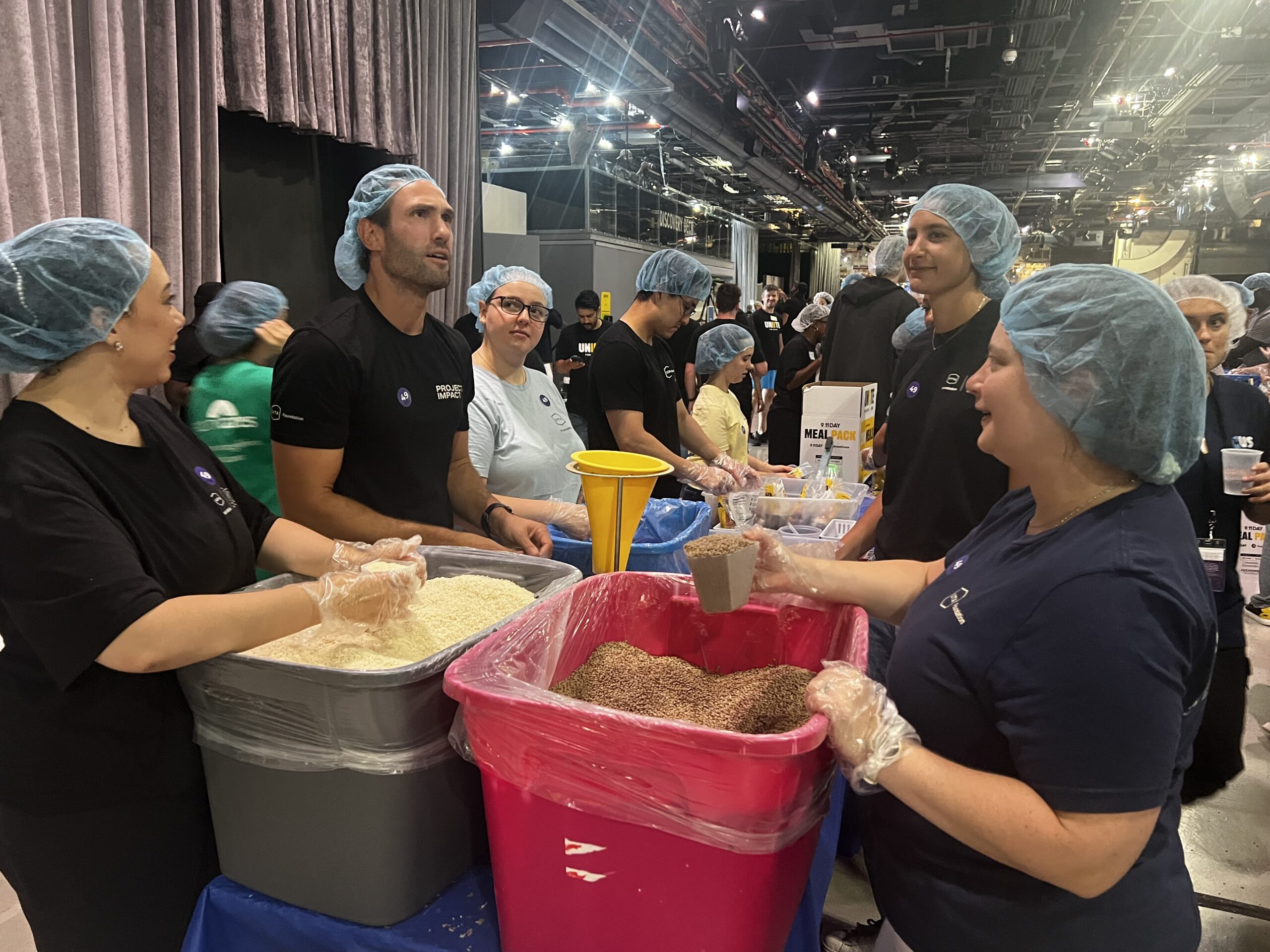Volunteers in hairnets and gloves packing meal ingredients into bins during the 9/11 Day of Service meal-packing event